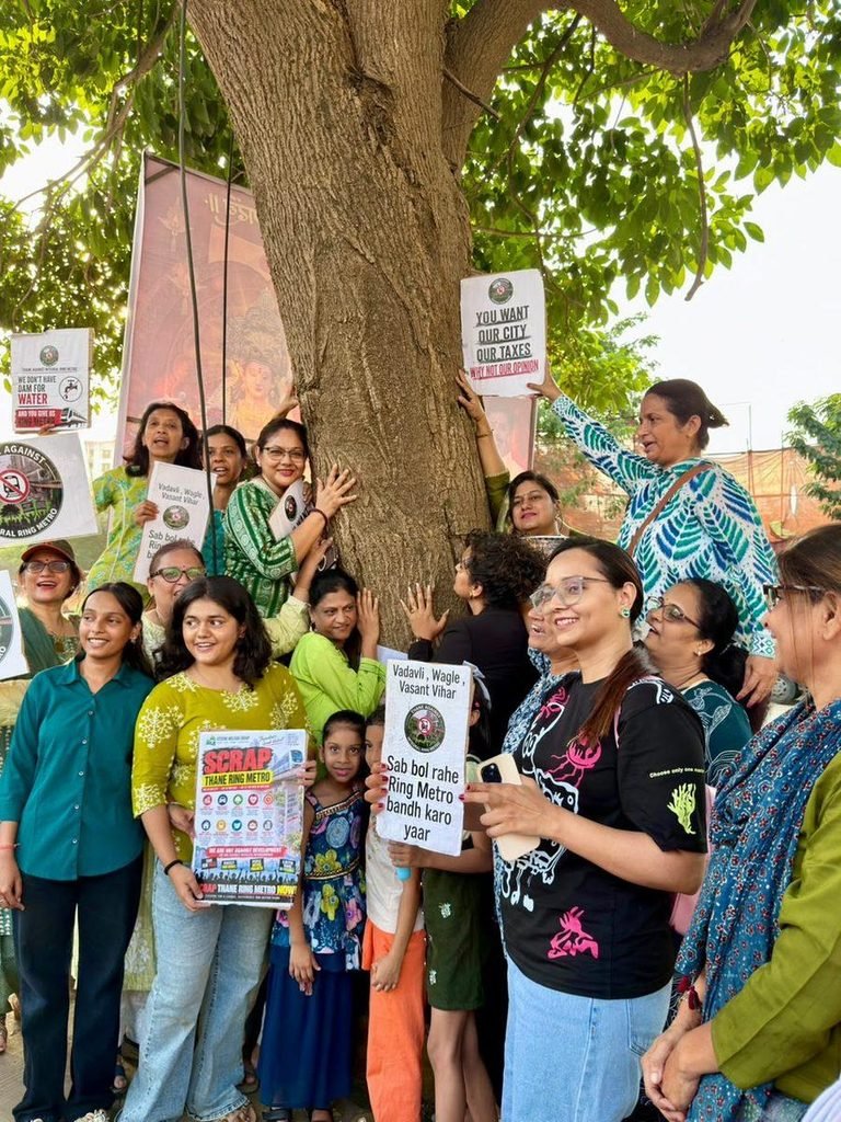 Women hug a large tree and hold placards reading “Scrap Thane Ring Metro” during a protest in Thane